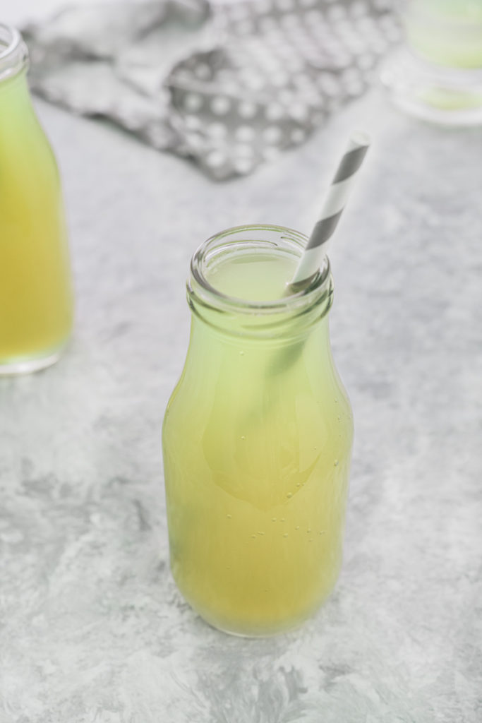 An open bottle of Sour Green Apple Soda, ready to sip with a grey and white striped straw.