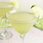 Martini glasses filled with vibrant green non-alcoholic appletinis with a slice of apple on the side of the glass.