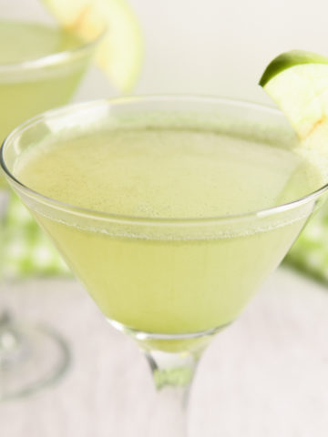 Martini glasses filled with vibrant green non-alcoholic appletinis with a slice of apple on the side of the glass.