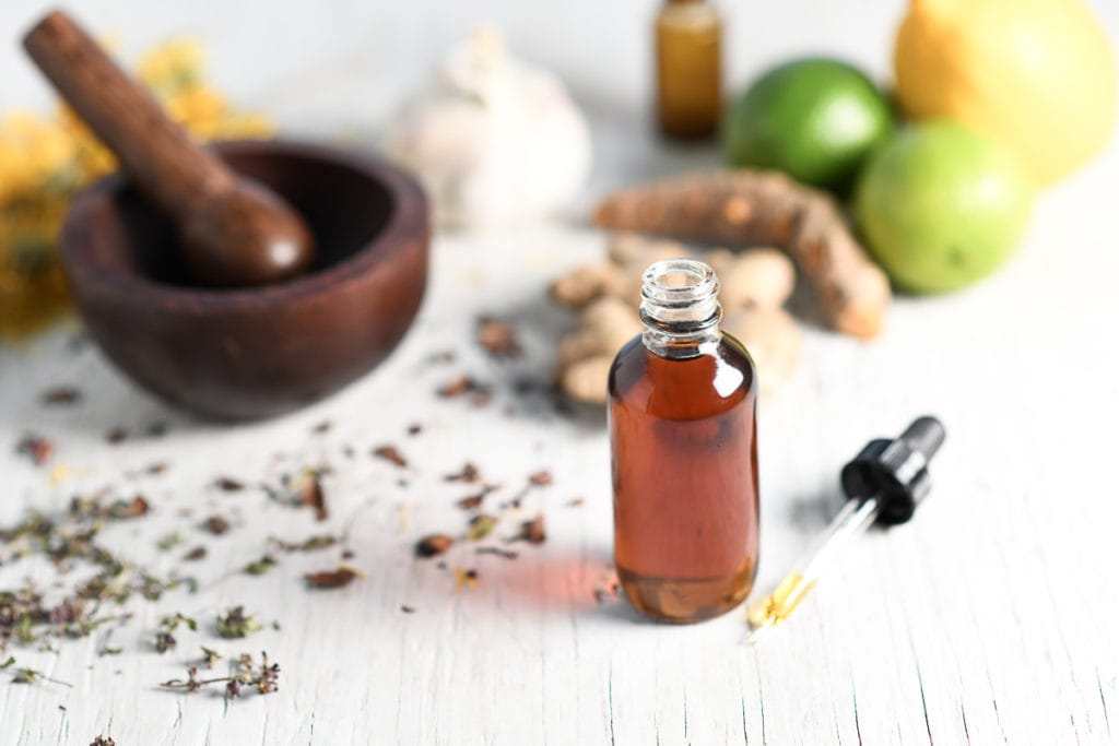 A tincture bottle, a pestle and mortar and citrus fruits, ginger, garlic and herbs.