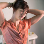 A woman with her eyes closed and her hands on the back on her head.