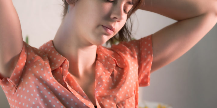 A woman with her eyes closed and her hands on the back on her head.