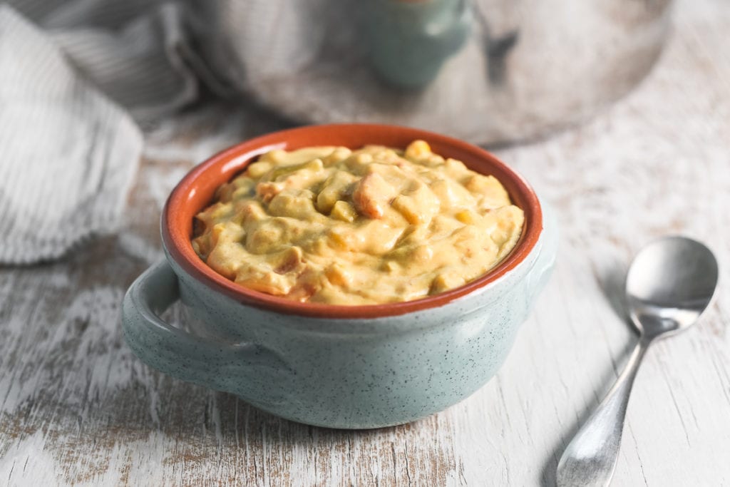 A big hearty bowl of creamy vegan sweet potato corn chowder in front of a large stock pot and linen cloth, with a silver spoon sitting beside.