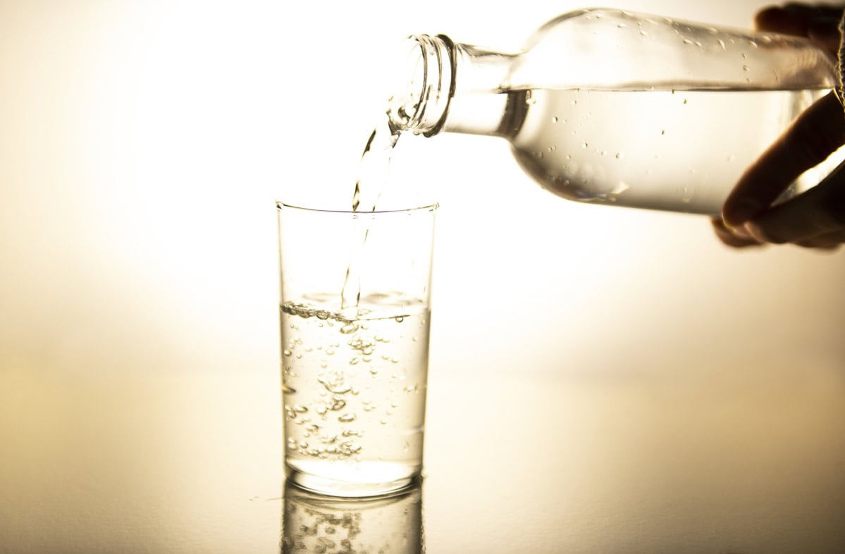 Water being poured from a glass bottle into a drinking glass.