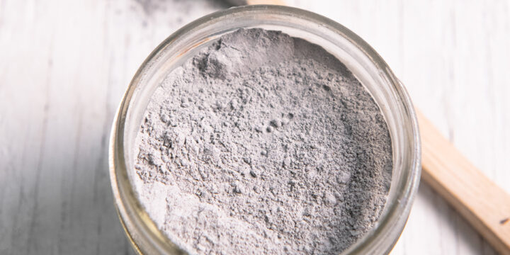 A quarter pint jar filled with charcoal toothpowder and a toothbrush that just been dipped in resting beside.