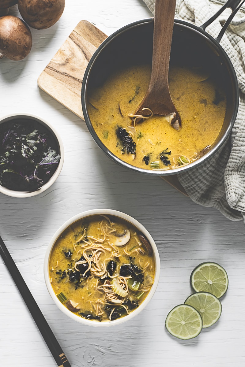  A bowl of Coconut Lime Soup loaded with vegetables and Thai noodles beside a pot with with leftovers.