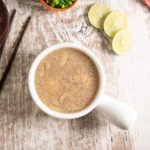 A bowl of hearty coconut soup with lime slices, green onion and a set of cop sticks.