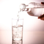 Water being poured out of a glass bottle into a drinking glass.
