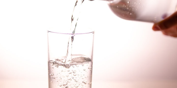 Water being poured out of a glass bottle into a drinking glass.