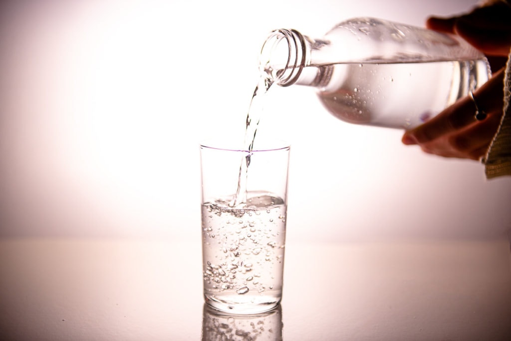 Water being poured out of a glass bottle into a drinking glass.