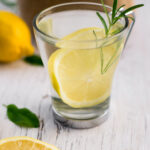 A clear mug with water, lemon and a sprig of rosemary,