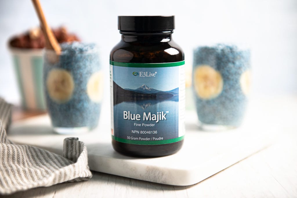 A bottle of Blue Majik Blue-green algae sitting in front of two cups of blue chia pudding.