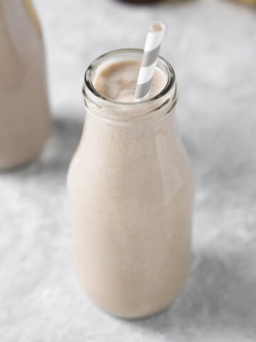 A cream coloured smoothie in a milk bottle with the tip of a white and grey straw peaking above the rim.