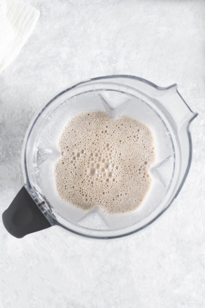 A freshly blended vanilla smoothie still in the blender jug with frothy bubbles on the top.