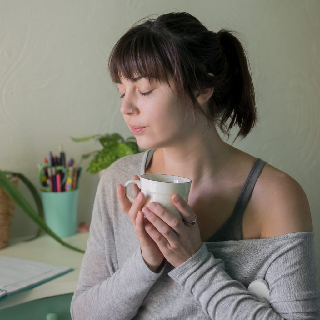 A young woman holding a mug close to her heart with her eyes closed and a content look on her face