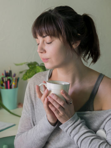 A young woman holding a mug close to her heart with her eyes closed and a content look on her face