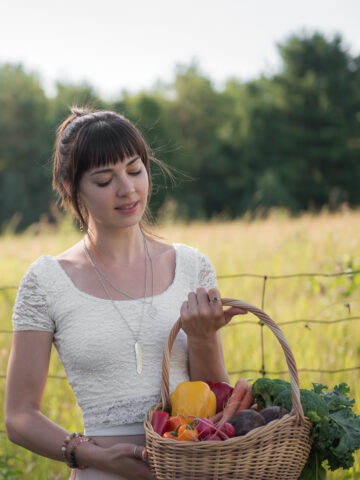 A girl holding a basket of fresh vegetables, looking very happy and healthy.