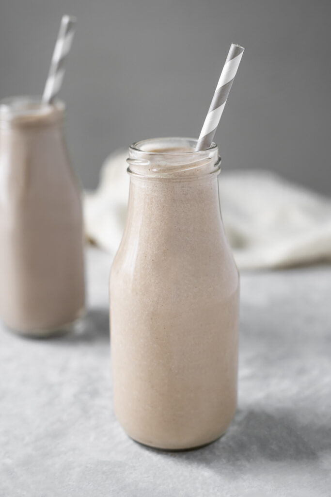 Two milk jars filled with vanilla smoothies diagonally placed in front of a white linen cloth.