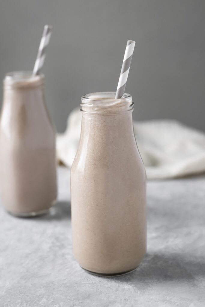 Two creamy, vanilla smoothies sitting diagonally with striped straws and linen cloth draped in the background.