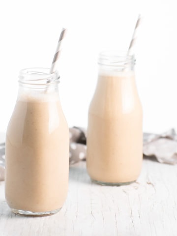 Two small milk jars filled with vanilla spice smoothies and a grey and white straw placed in each.