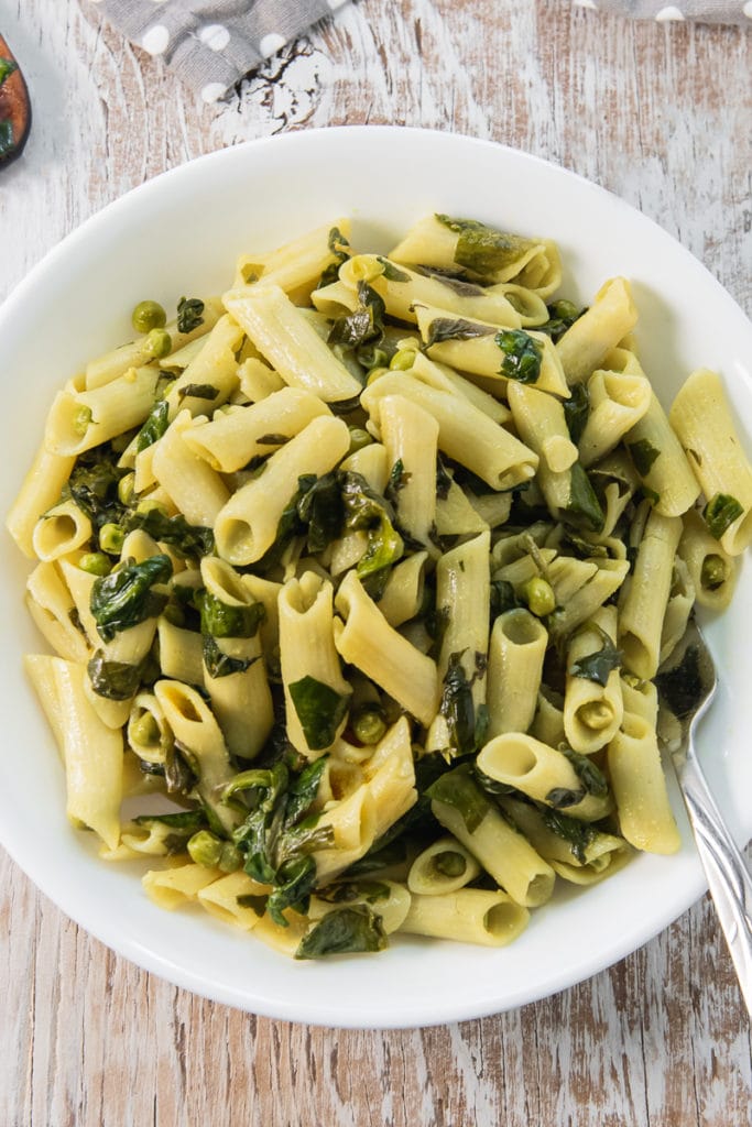 A close up of a heaping bowl of delicious Spinach and Peas Penne Pasta with a fork in the bowl.