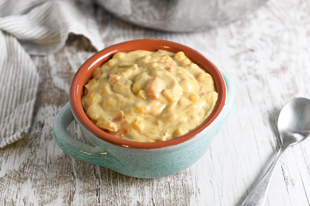 A french onion soup bowl filled with a creamy sweet potato corn chowder with a spoon and linen cloth to the side.