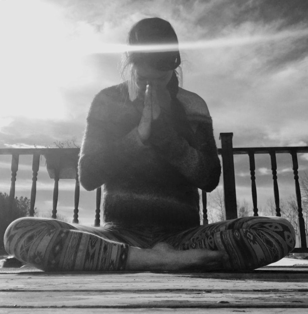 A woman sitting cross-legged bowing in prayer position.