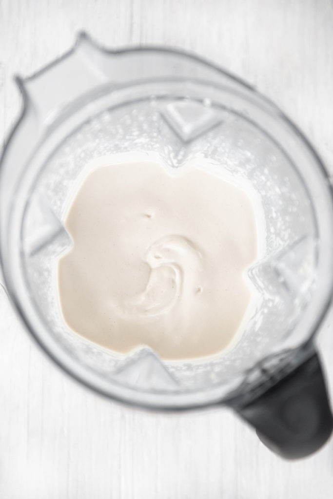 Smooth, white cashew cream, freshly blended in a blender jug with spatters up the slides.