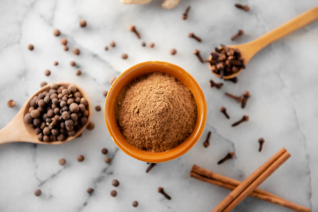 Bowl of Homemade Pumpkin Pie Spice surrounded by cinnamon sticks, cloves and allspice.