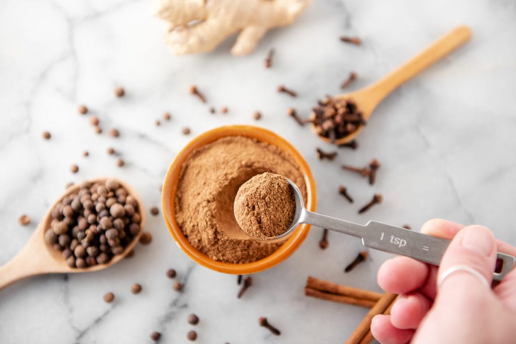 A teaspoon of pumpkin pie spice being lifted above a full bowl full.