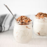 Two jars filed with peaches and cream, topped with crunchy granola.