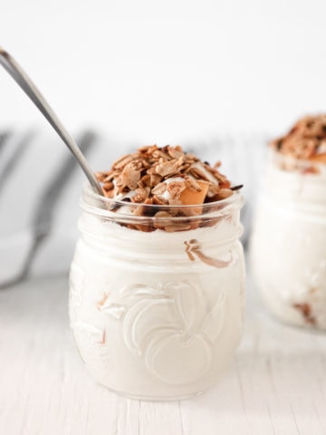 Two jars filed with peaches and cream, topped with crunchy granola.