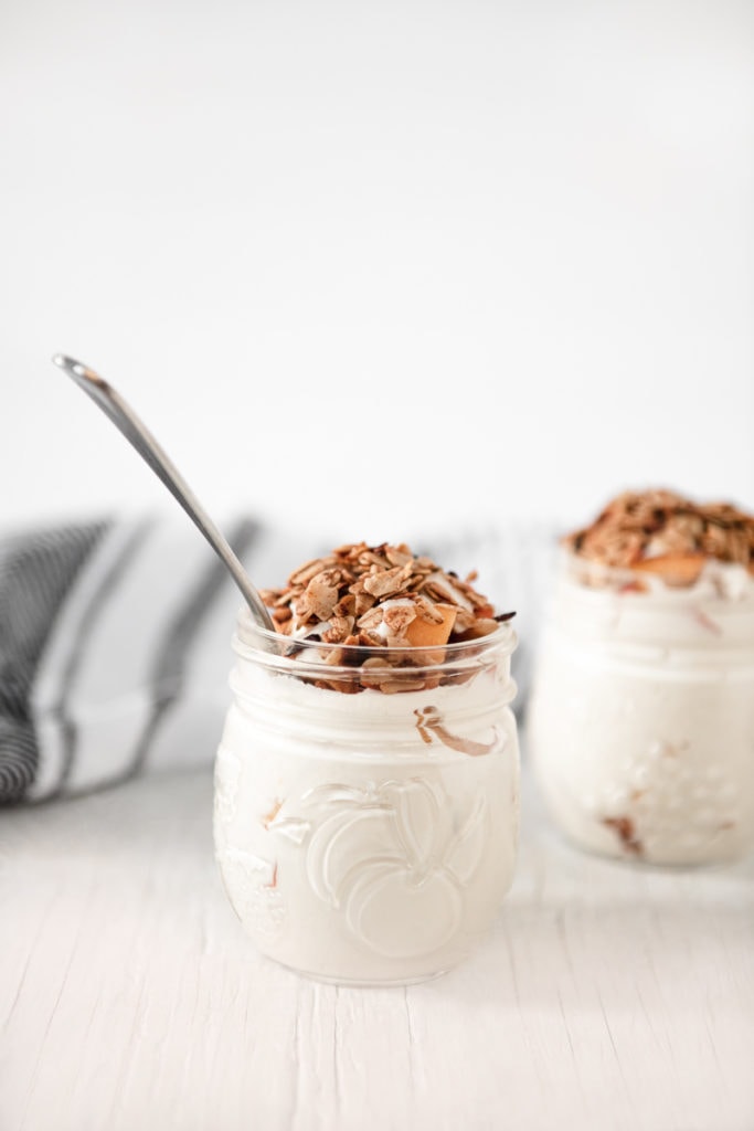 Two jars filed with peaches and cream, topped with crunchy granola.