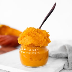 Homemade Pumpkin Purée heaping out of a glass jar with a wooden spoon sticking out the top.