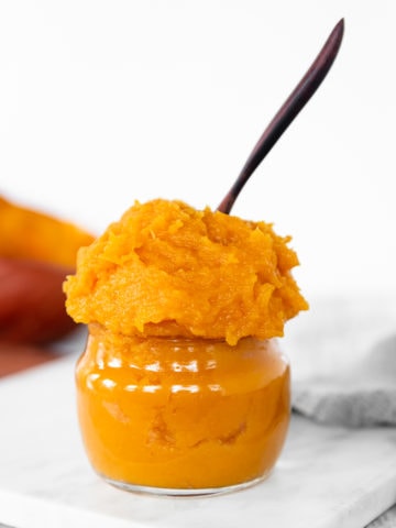 Homemade Pumpkin Purée heaping out of a glass jar with a wooden spoon sticking out the top.