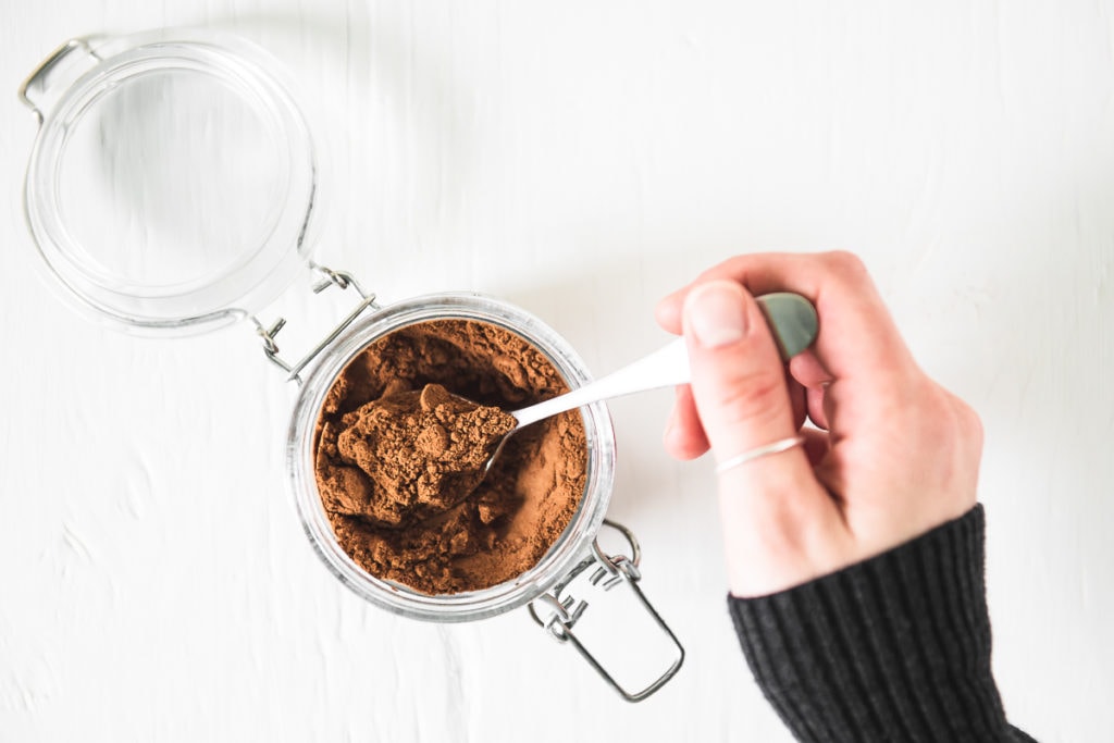 A hand scooping out a spoonful of caffeine-free french vanilla powder from a glass jar with a latch lid