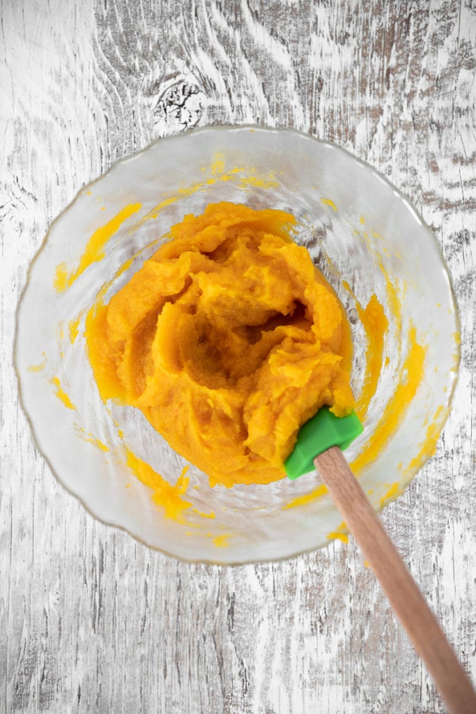A bowl of puréed pumpkin being stirred with a spatula.