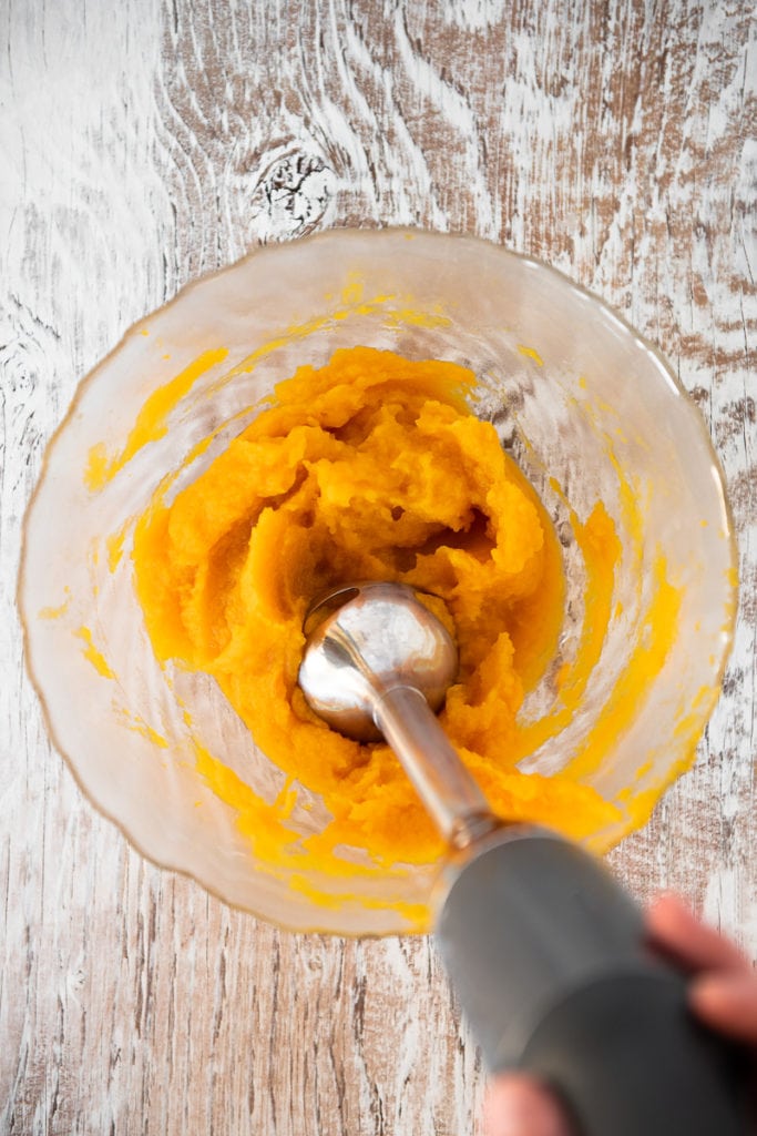 A bowl of cooked pumpkin being puréed with an emersion blender.