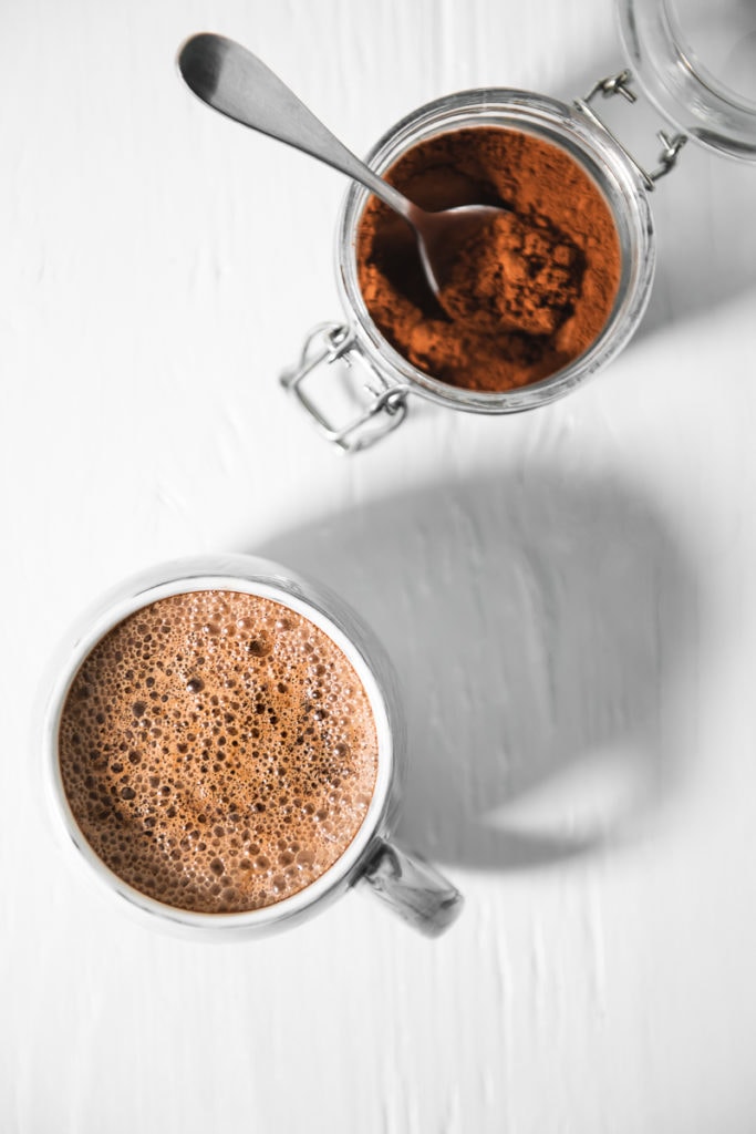 A frothy, freshly made Vegan French Vanilla Cappuccino beside an open jar of Homemade French Vanilla Mix.