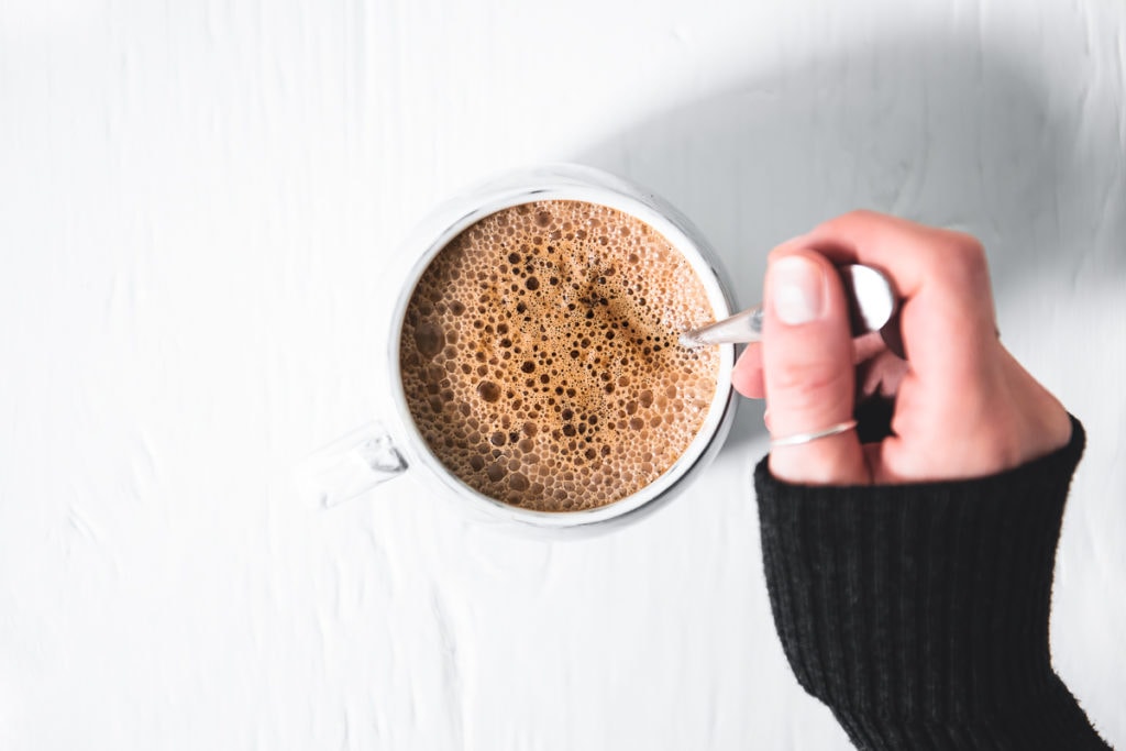 A hand stirring a frothy vegan french vanilla cappuccino