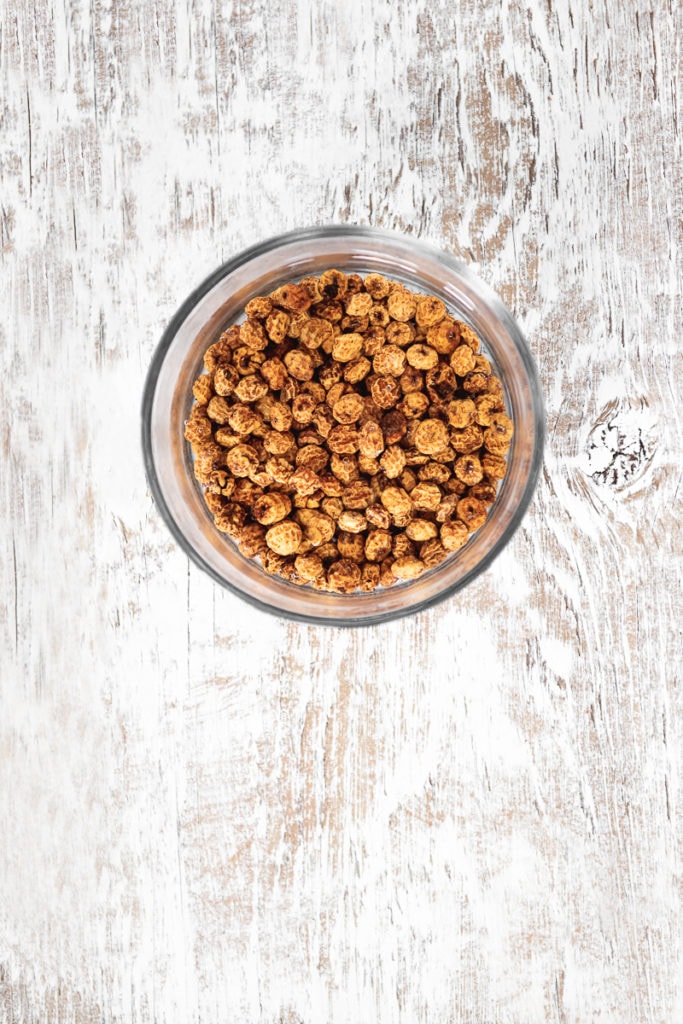 Tigernuts (chufas/nutsedge) soaking in a bowl of water on a white-washed wooden table top.