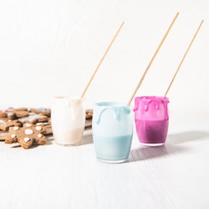 Three jars of naturally coloured icing with decorating sticks and icing dripping down the sides and a plate of gingerbread cookies beside.