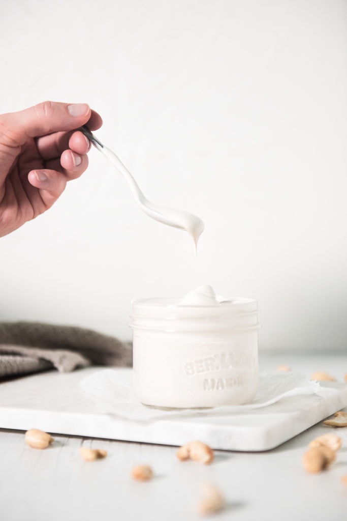 dripping spoonful of cashew cream being scooped out of a jar.