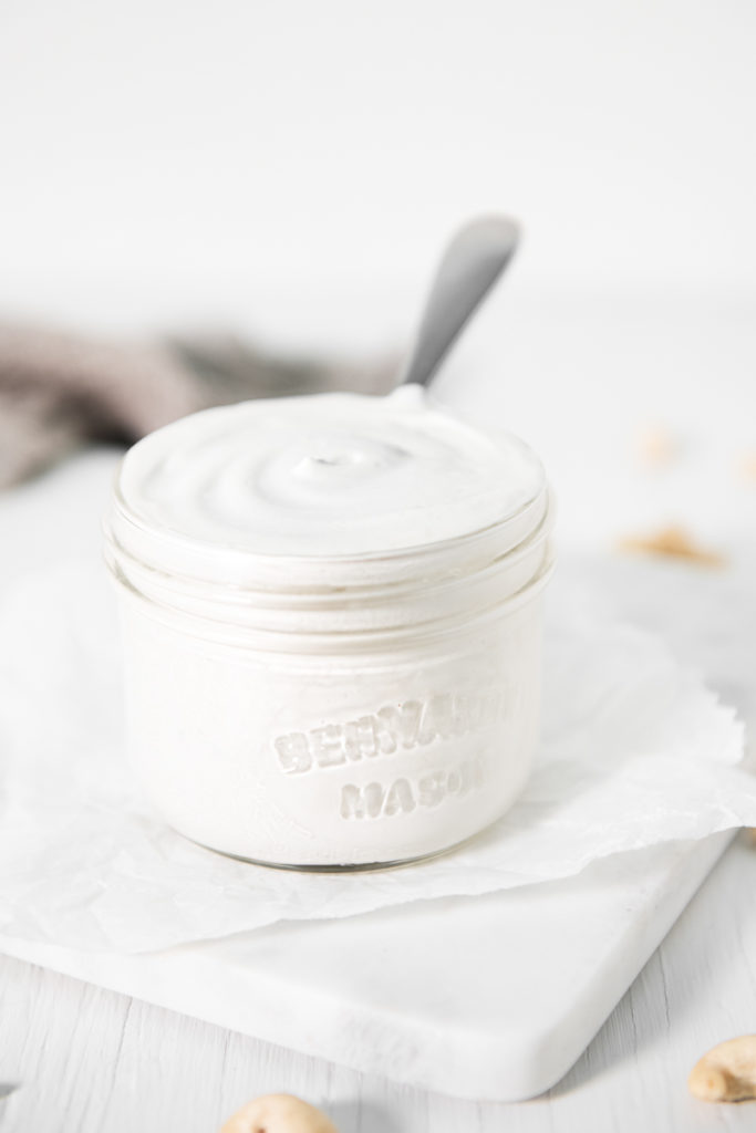 A jar of freshly made cashew cream with a spoon dipped in.