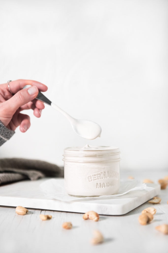 A spoonful of cashew cream being scooped out of a jar.