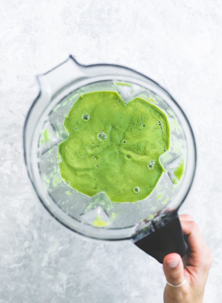 A hang grabbing the handle of a blender jug filled with a freshly blended, vibrant green smoothie.
