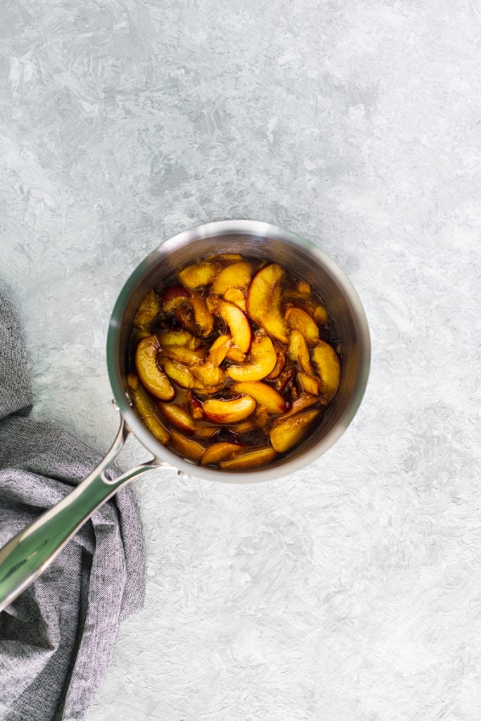 A saucepan filled with freshly made peach pie filling and a linen cloth laying underneath the handle.