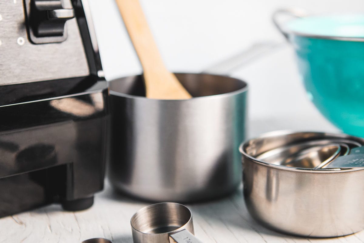 The bottom of a blender, measuring spoons, a stack of measuring cups, a colander and a small pot with a wooden spoon sitting in it.