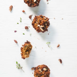 Sweet Potato Muffins laying in a staggered row sprinkled with toasted almonds, thyme and surrounded by crumbs.