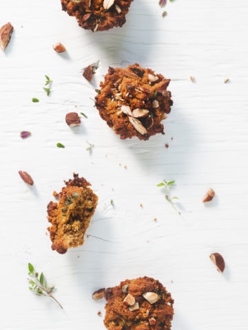 Sweet Potato Muffins laying in a staggered row sprinkled with toasted almonds, thyme and surrounded by crumbs.
